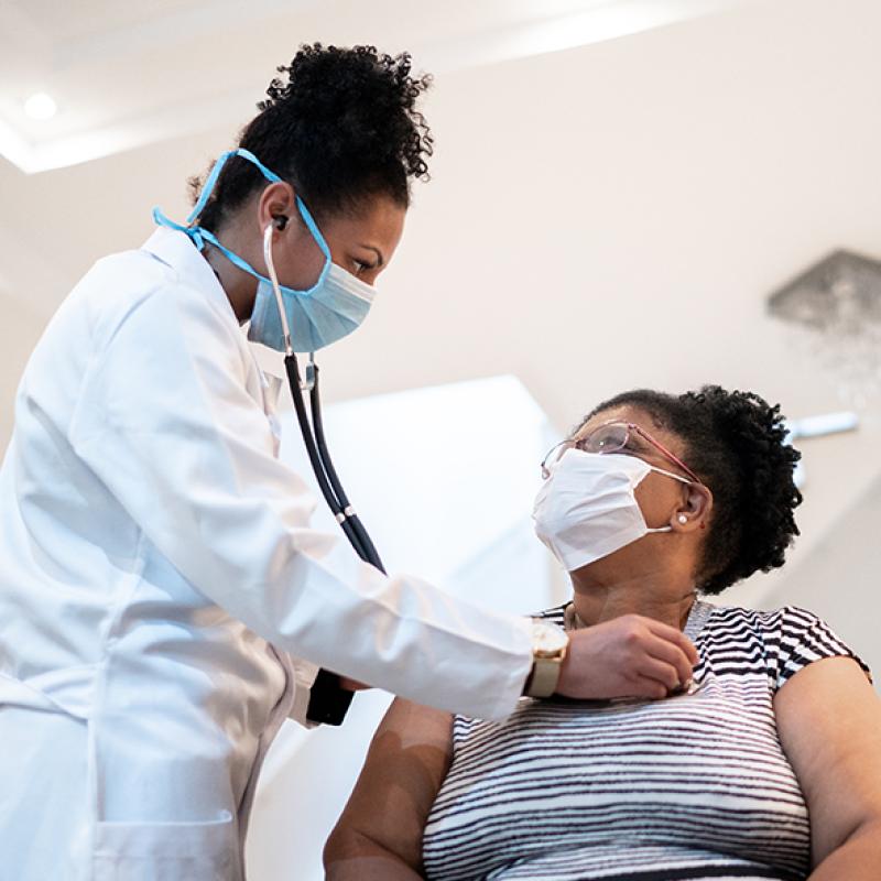 Black doctor holding a stethoscope to the chest of a Black patient