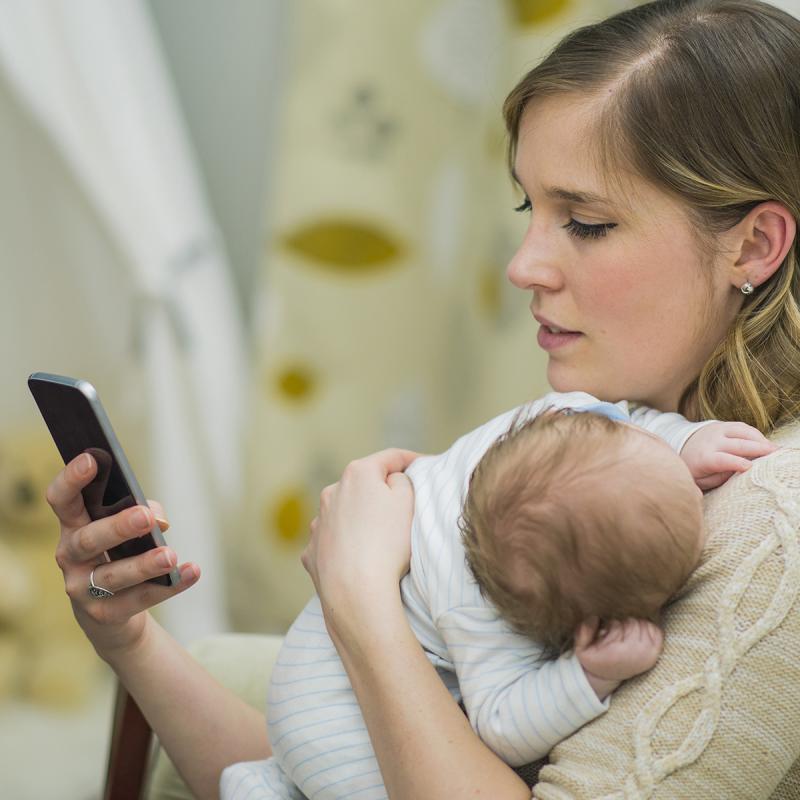 Mother holding an infant and looking at cellphone