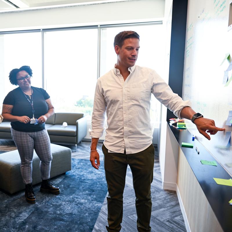 Kit Delgado points at text on a whiteboard. A team member watches on the side.