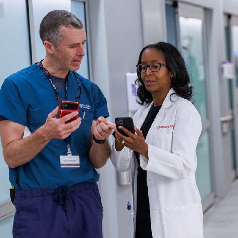 Raina Merchant shows her cell phone to a colleague in scrubs 