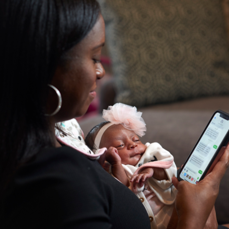 Mother holding an infant and looking at cellphone