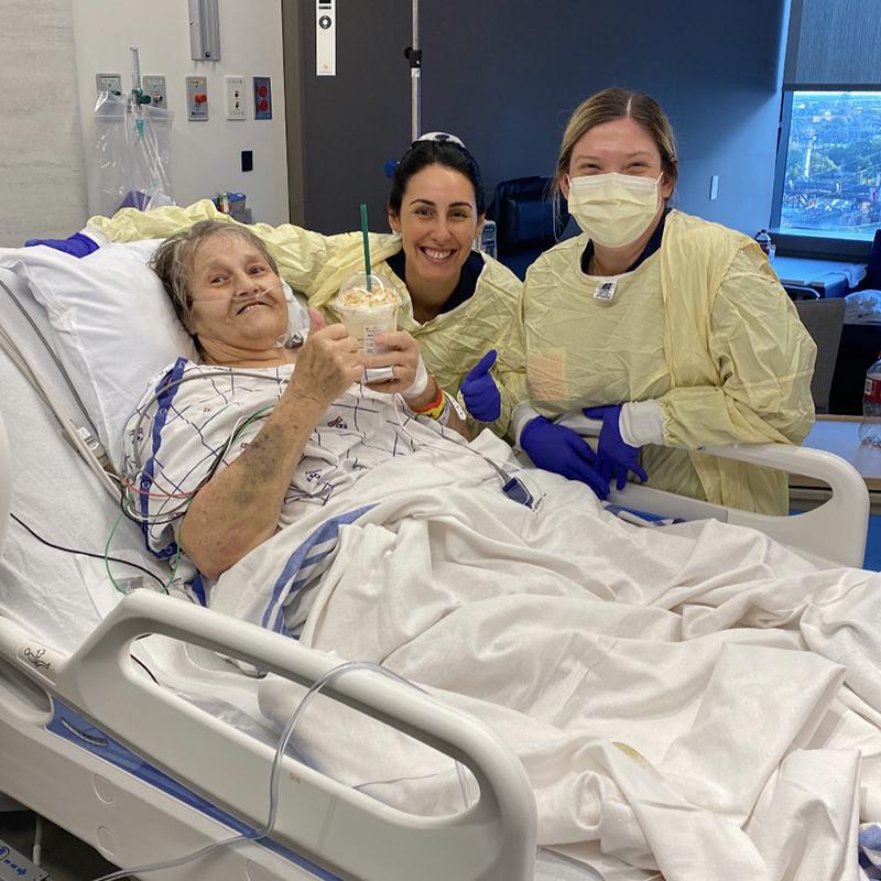 Two nurses stand beside a hospital patient holding a Starbucks drink she was gifted