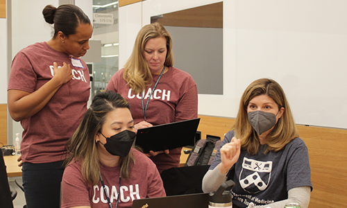 Three EHR coaches work on their computers while a hackathon participant makes a point