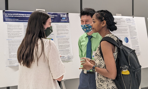Three people stand next to a research poster