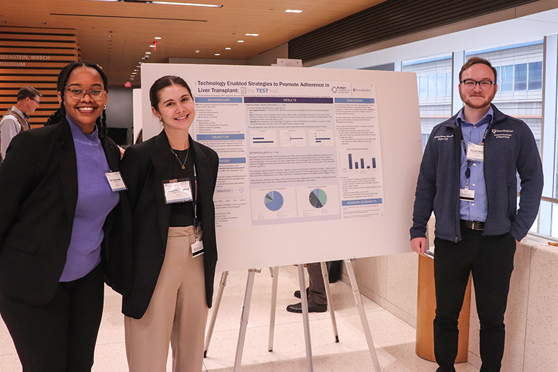 Three smiling attendees pose in front of a research poster