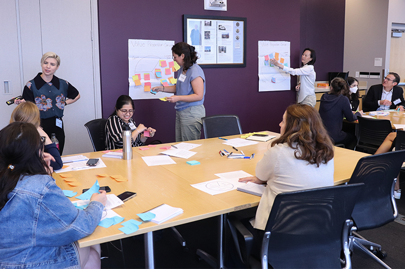 Service design workshop attendees place sticky notes on the wall